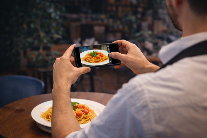Waiter taking a photo of a dish with their phone for the restaurant digital menu